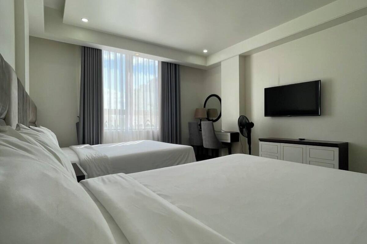 A hotel room with two beds, a desk, a chair, a TV, and a window with curtains.