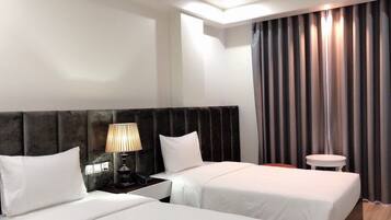 A hotel room with two beds, a nightstand with a lamp, a small table, and a large window with curtains.