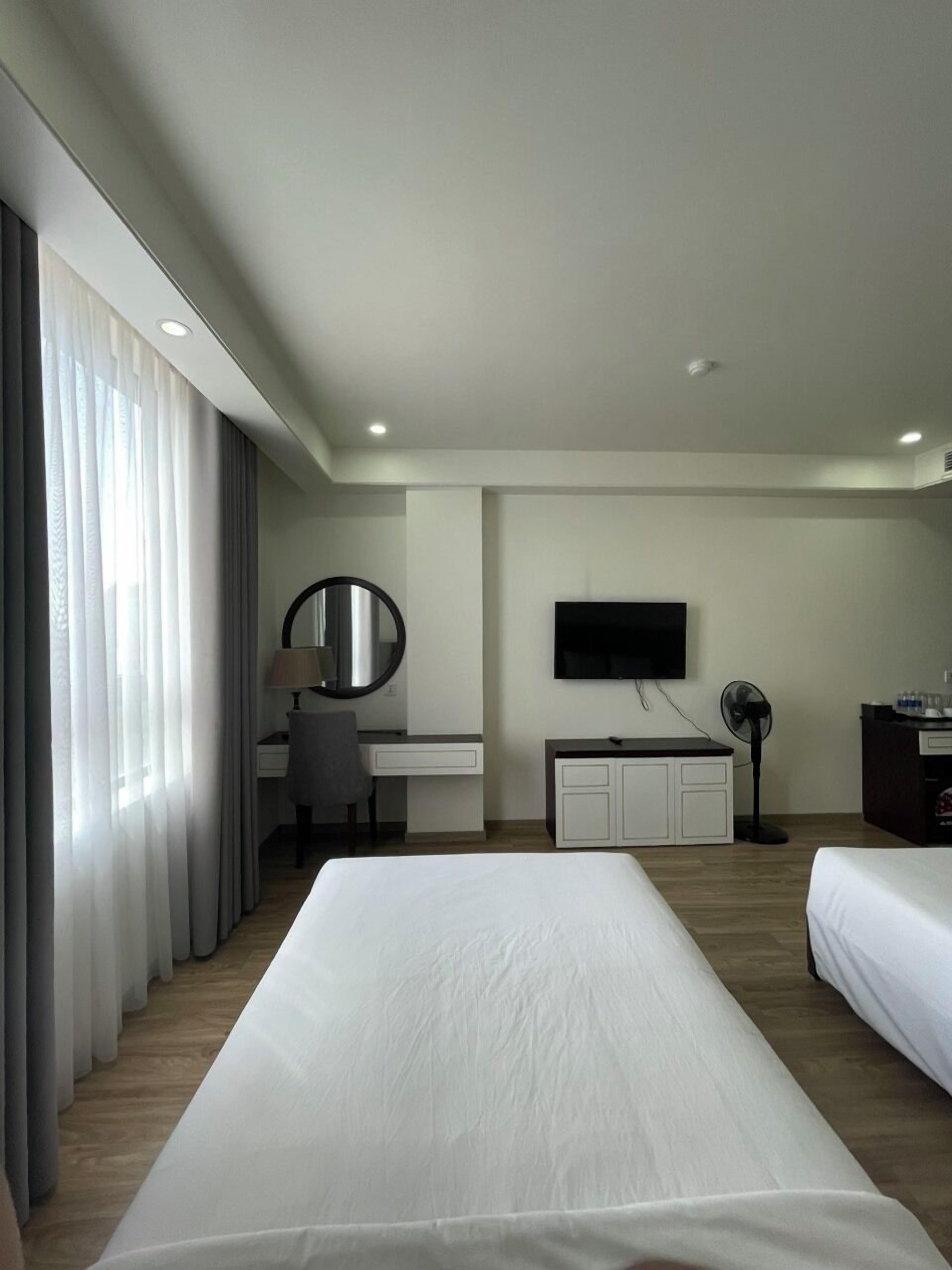 A hotel room with two beds, a desk with a chair, a television, and a desk lamp.