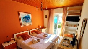 A hotel room with two beds, a desk, a chair, a TV, and a balcony with curtains. - Villa "Eva" - Entire Beachwalk Holiday Home - 4 Seasons & Longer Stays (Agios Dimitrios)