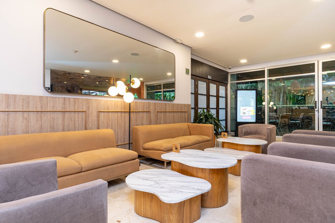 A modern lobby with sofas, marble coffee tables, and a large mirror.