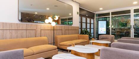 A modern lobby with sofas, marble coffee tables, and a large mirror.