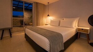Un dormitorio moderno con una cama grande, una mesita de noche, una lámpara, una pequeña mesa y una puerta corrediza de cristal que da a un espacio exterior.