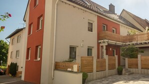 En toetages boligbygning med en facade i rødt og hvidt, et tegltag og en belagt gårdsplads.