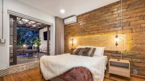 A modern bedroom with a brick wall, a large bed with a fluffy white cover, and a wooden floor. - Casa Madera · Casa Madera Parque Lleras 7BR with private Jacuzzi (Medellín)