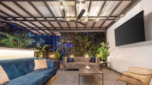 An outdoor seating area with a sofa, armchair, and coffee table, surrounded by plants and a large screen. - Casa Madera · Casa Madera Parque Lleras 7BR with private Jacuzzi (Medellín)
