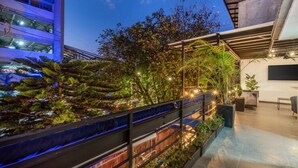 A rooftop garden with a variety of plants and trees, a modern building with a glass facade, and a seating area with a table and chairs. - Casa Madera · Casa Madera Parque Lleras 7BR with private Jacuzzi (Medellín)