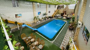 Un área de piscina interior con una piscina azul, rodeada de césped artificial verde, mobiliario de mimbre y plantas en macetas.
