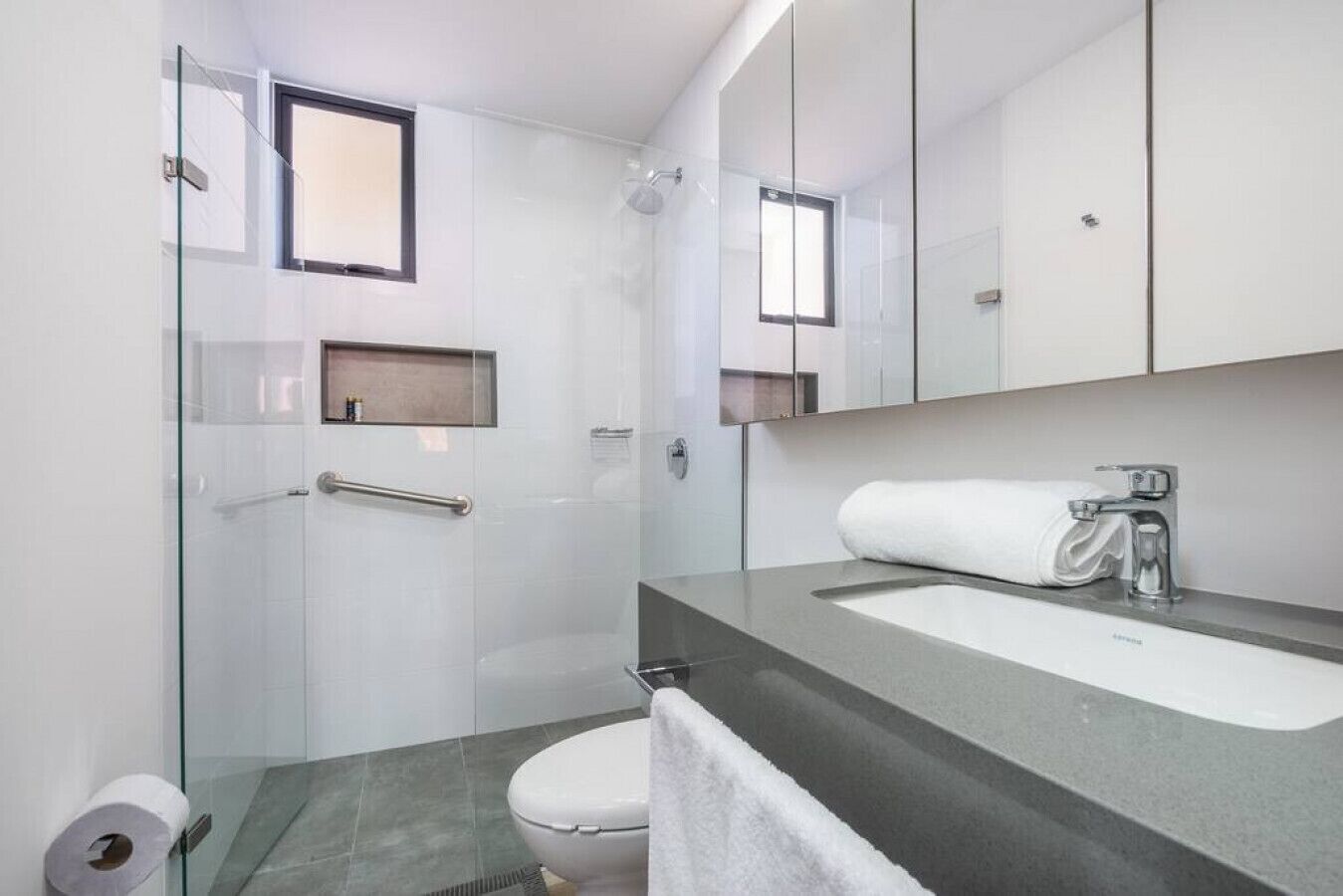 Un bagno moderno con doccia vetrata, un water bianco e un lavandino capiente con uno specchio sopra.