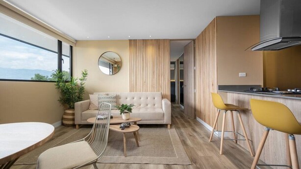 Una sala de estar moderna con sofá, mesa de centro y sillas, una cocina con estufa y un ventanal con vistas amplias.