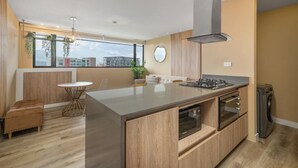 Cocina moderna con una isla central, horno empotrado y microondas. Cuenta con un comedor con mesa redonda y sillas, además de un pequeño rincón de estar con un banco acolchado.