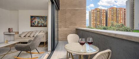 A balcony with a sofa, two chairs, a small table, and two wine glasses.