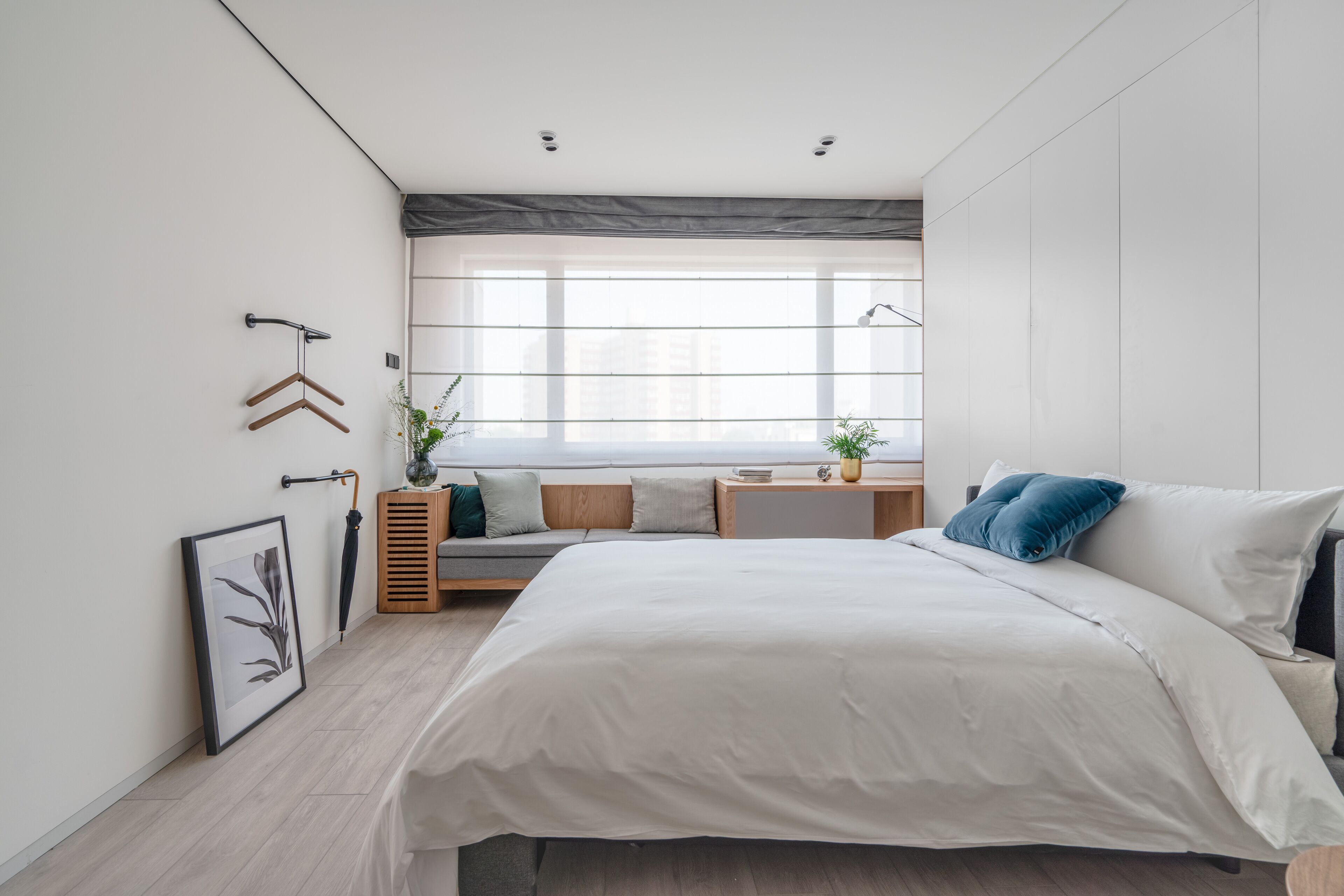 A modern bedroom with a large bed, a bedside table, a window, and a wall-mounted coat rack.