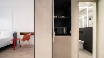 Een moderne hotelkamer met een bed, een klein rode tafel, een rode stoel en een kitchenette met een magnetron.