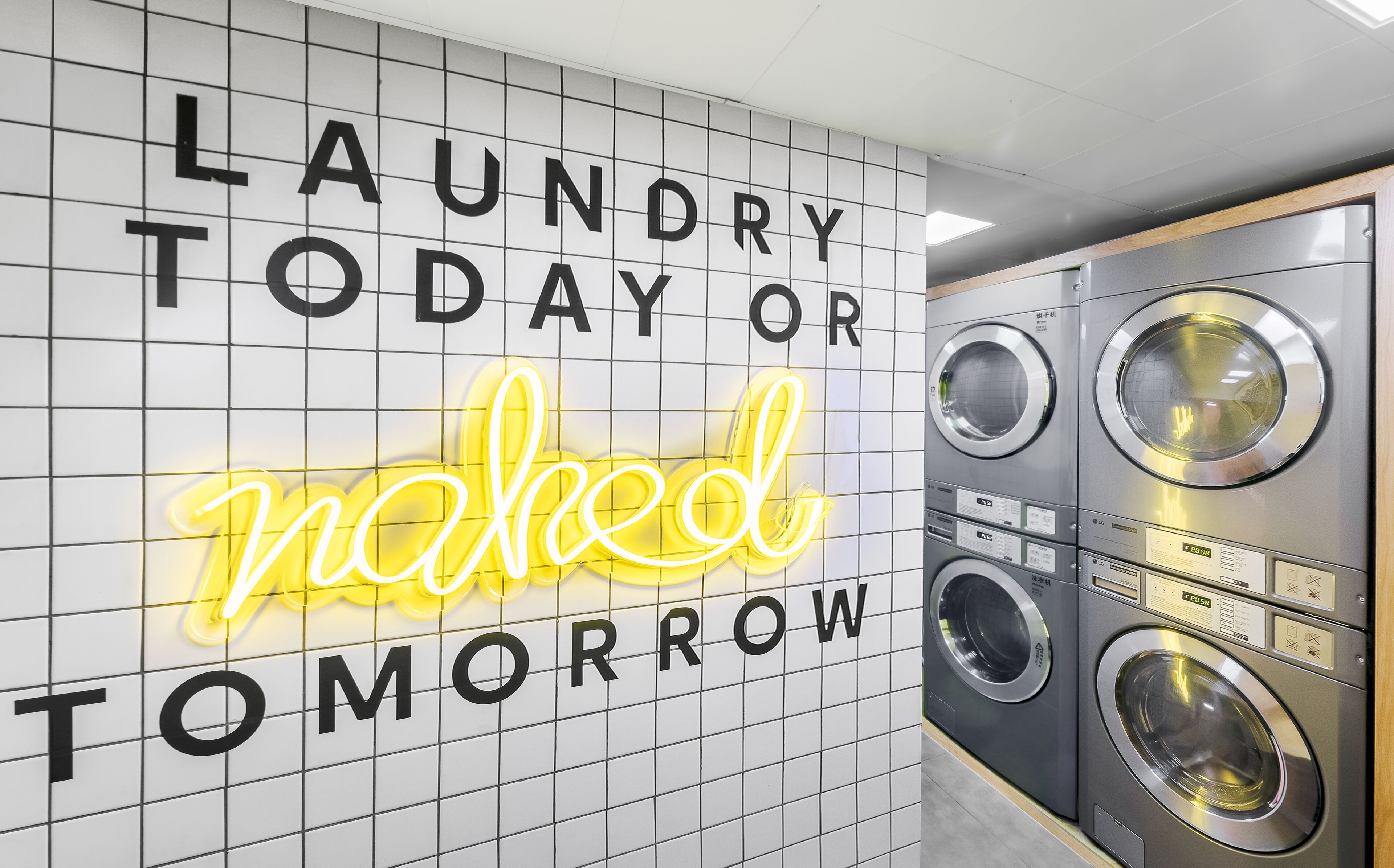 A laundry room with a neon sign that reads "LAUNDRY TODAY OR NAKED TOMORROW".