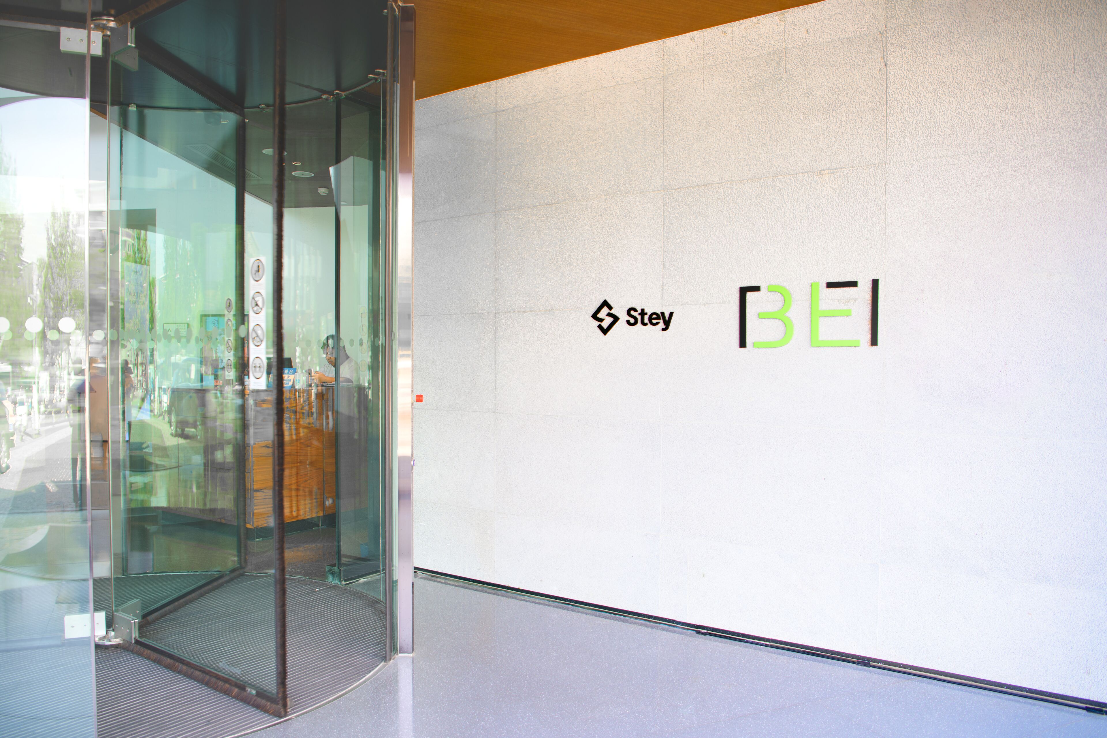 A glass door entrance to a building with the logo 'Stey BEI' on the wall.