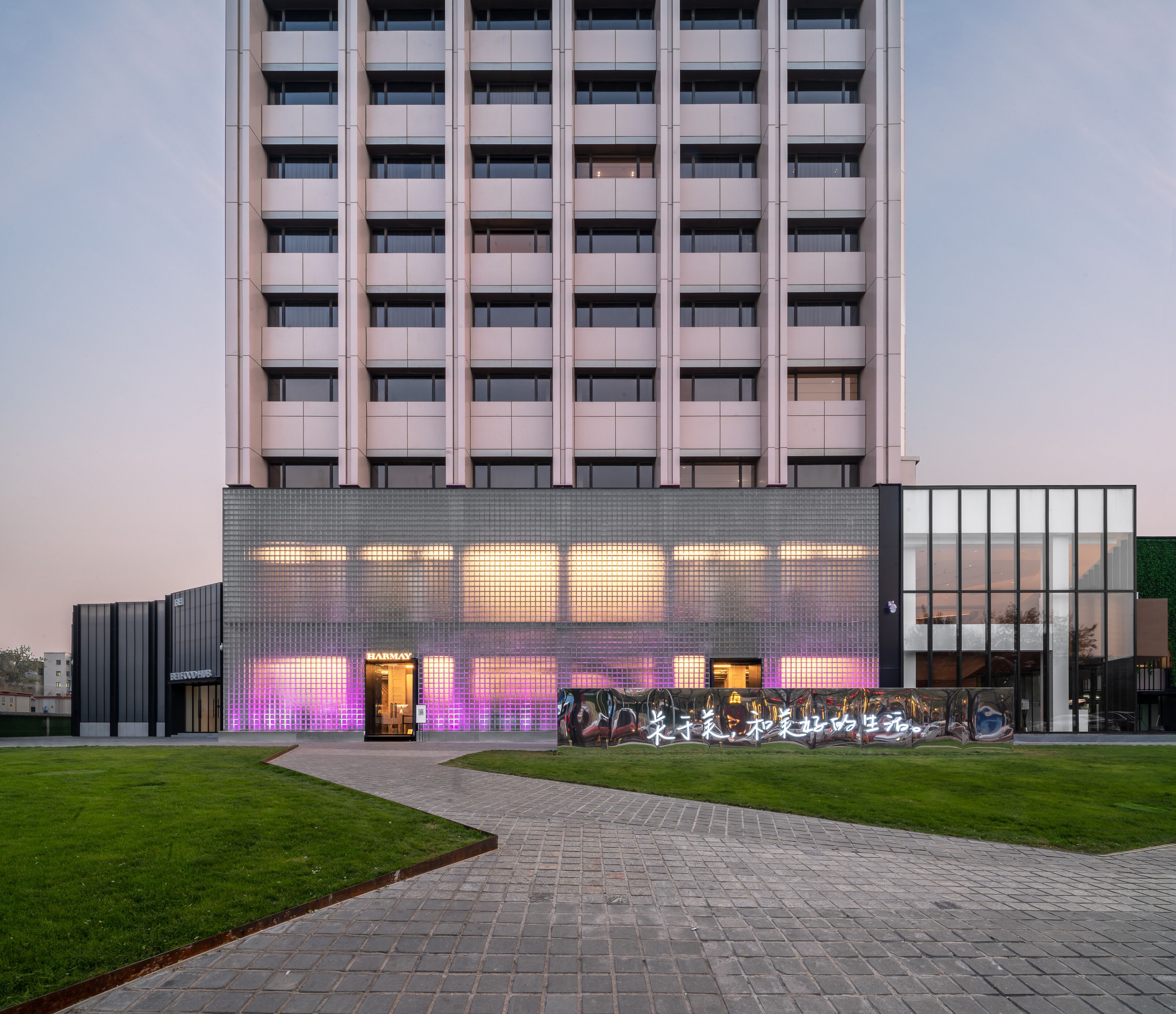 A modern building with a glass facade, a visible entrance, and a paved pathway leading to it.