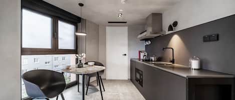 A modern kitchen with a dining area, large windows, and a view of buildings outside.