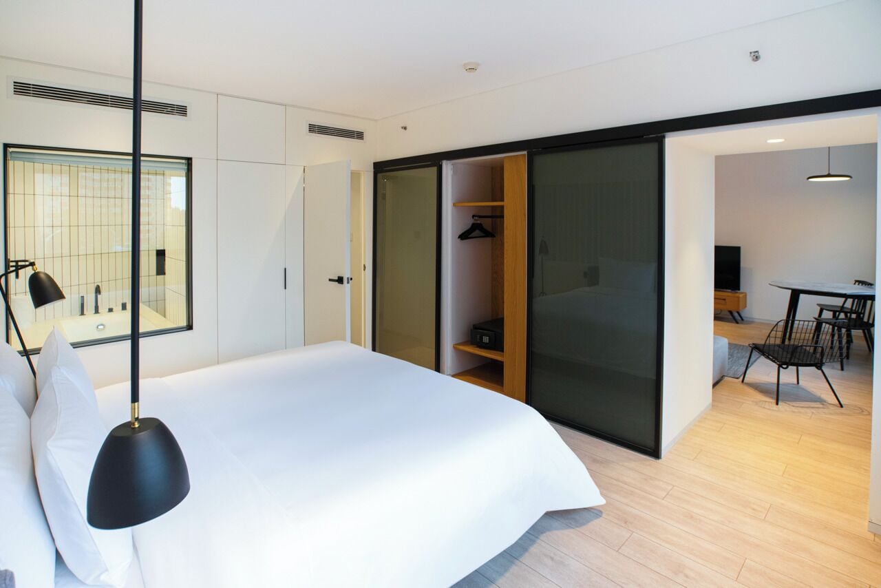 A modern bedroom with a large bed, a wardrobe, and a dining area.