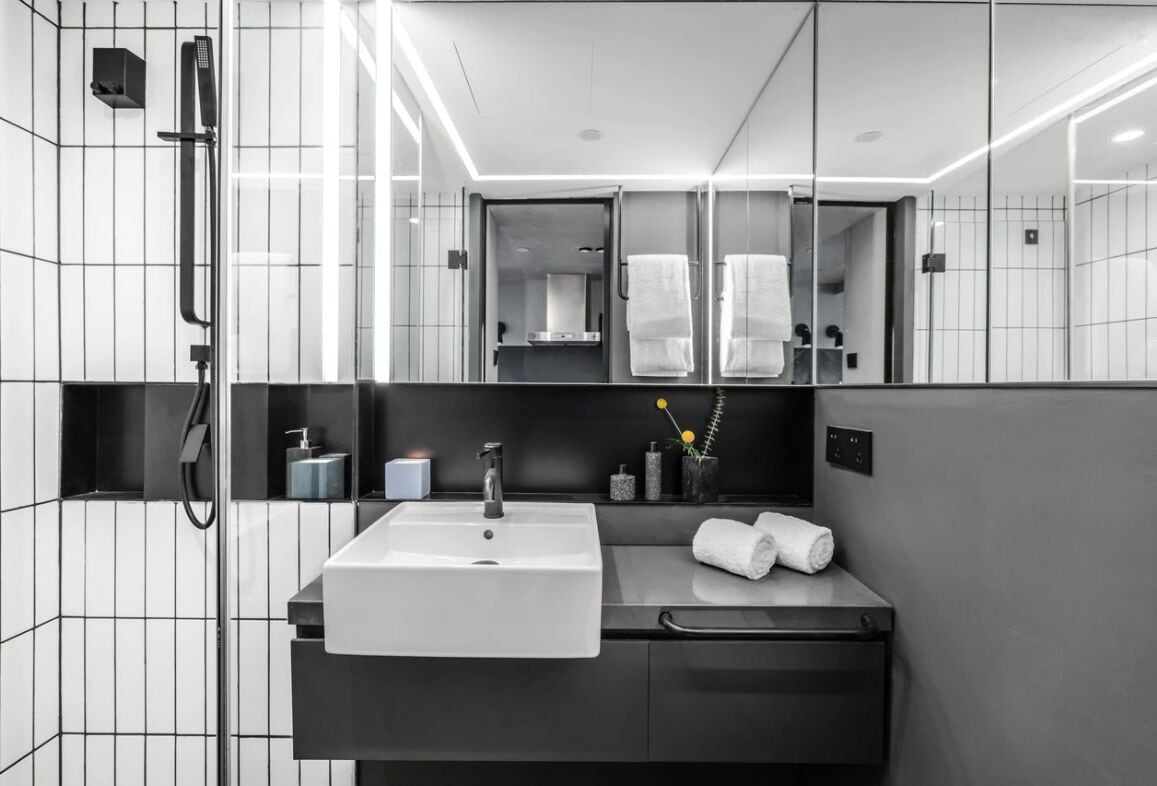 A modern bathroom with a large mirror, a white sink, and a shower area.