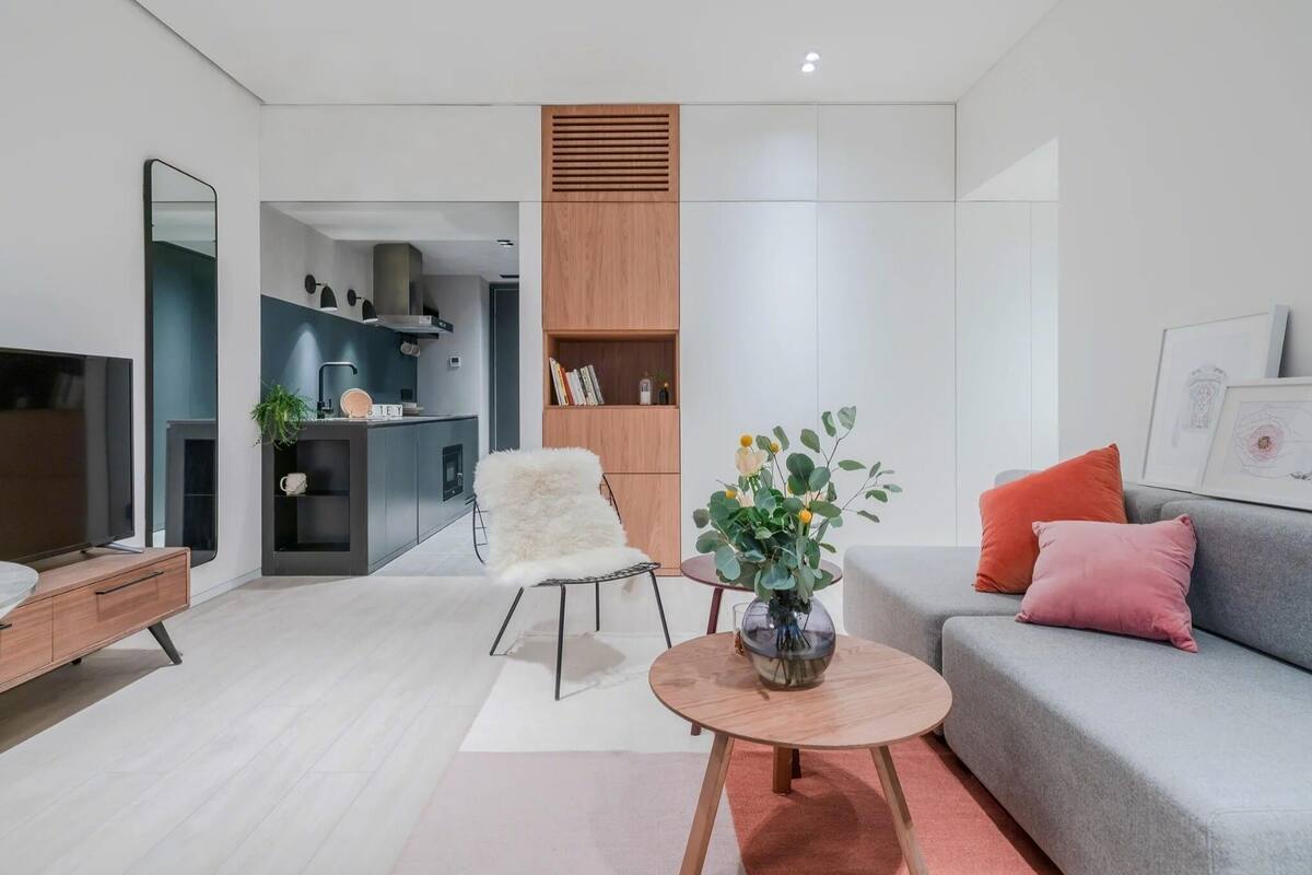 Un salon moderne avec un canapé, une table basse, un fauteuil moelleux et un coin repas, la cuisine étant visible au fond.