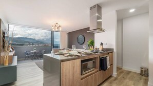 A modern kitchen with a central island, a dining area with a view, and a large window. - Go Living 708 · Luxury Apt-balcony and city view-AC and coworking (Medellín)