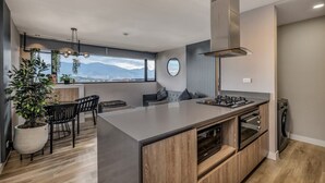 Une cuisine moderne dotée d’un îlot central, d’un four encastré et offrant une vue sur les montagnes grâce à de grandes fenêtres.