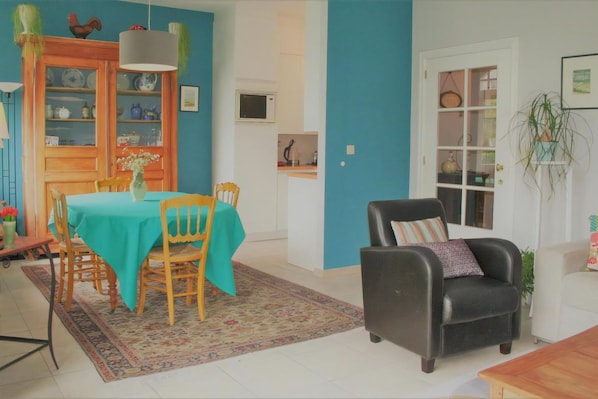 Un coin repas avec une table dressée pour quatre personnes, un fauteuil en cuir noir, un canapé blanc et un buffet en bois contenant de la vaisselle.
