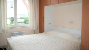 Un dormitorio con cama, ventana con cortinas, radiador y paneles de madera en la pared.