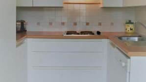 Una cocina compacta con armarios blancos, una encimera, una estufa y un fregadero.