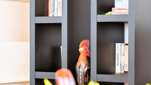 Una estantería con libros y objetos decorativos, una figurita de gallo y un florero con flores.