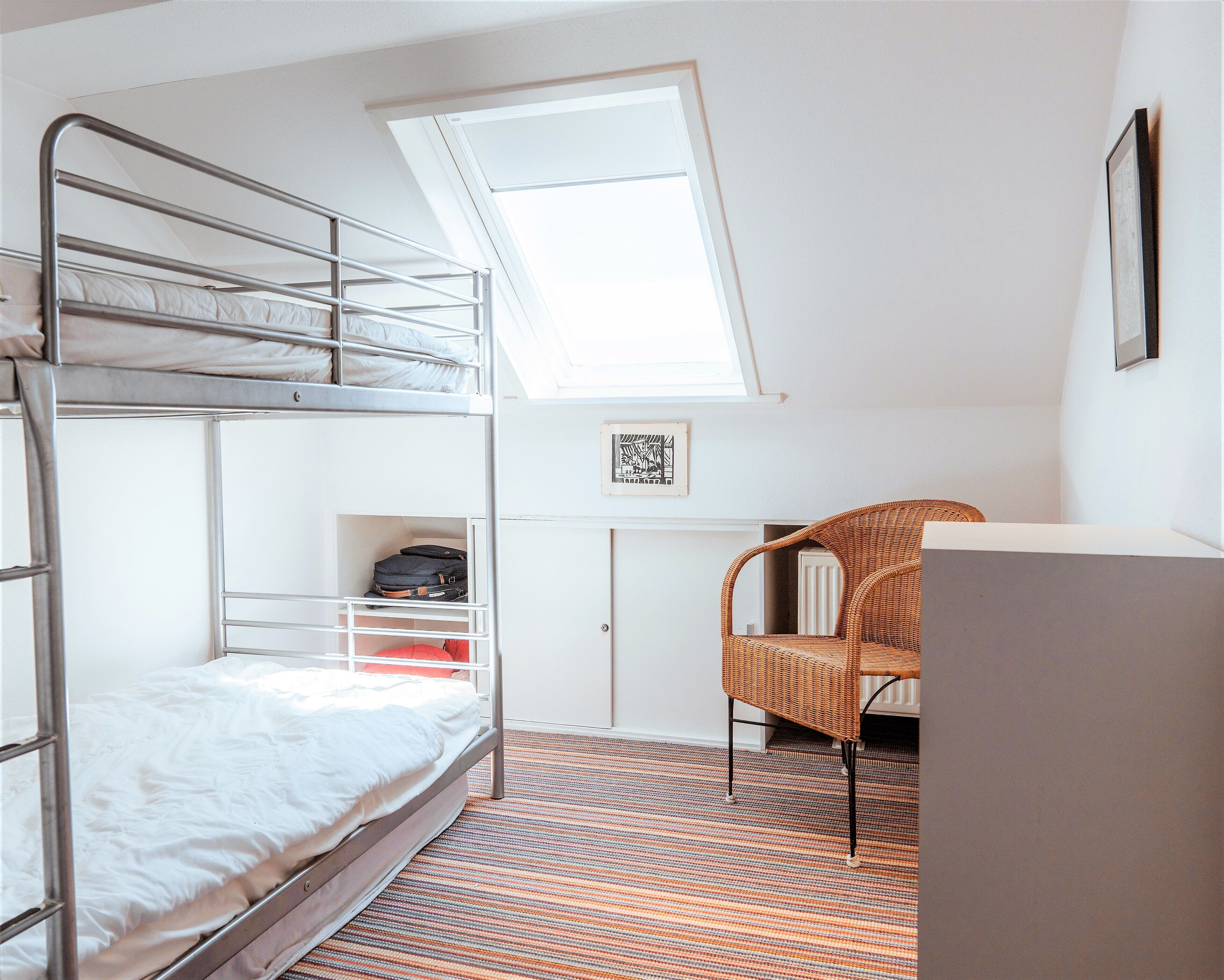 A compact room with bunk beds, a wicker chair, a desk, and a skylight.