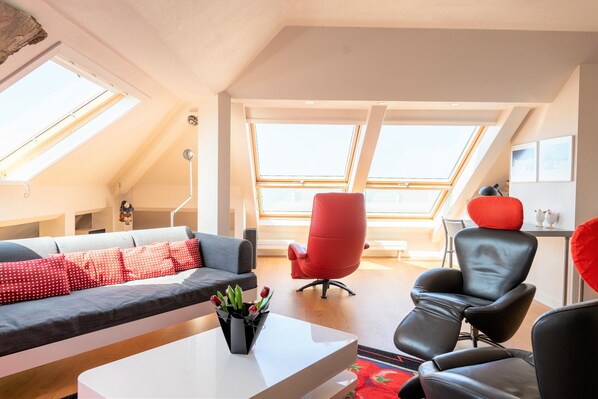 A modern living room with a sofa, red chairs, a coffee table, and skylights.