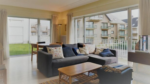 Un salon moderne avec un canapé, une table basse et un balcon offrant une vue sur d’autres immeubles.
