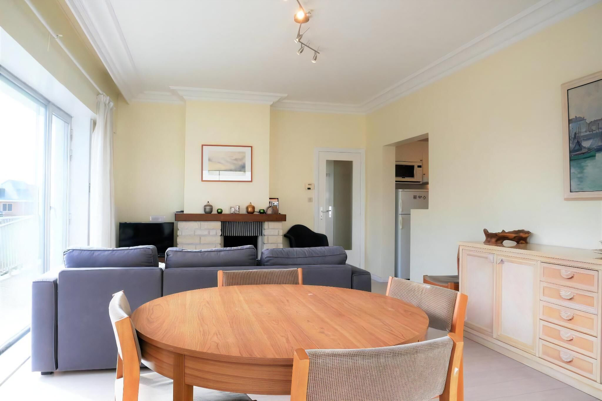 Een woonkamer met een ronde houten tafel, grijze banken en een televisie.