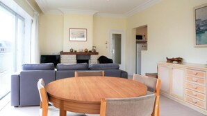 Un salon avec une table ronde en bois, des canapés gris et un téléviseur.