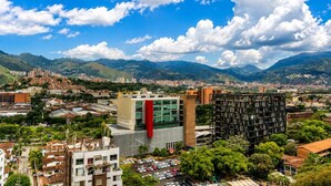 A cityscape with modern buildings, a prominent red and white structure, and a mountainous backdrop.