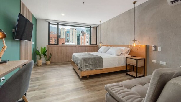 Une chambre moderne équipée d’un lit, d’un bureau, d’une chaise, d’un téléviseur et offrant une vue sur le paysage urbain.