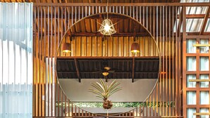 Una habitación con techo curvo, listones de madera, una cama con colcha gris, una planta en maceta y dos lámparas colgantes.