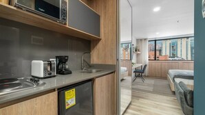 Une petite cuisine équipée d’un four à micro-ondes, d’un grille-pain, d’une machine à café et d’un lave-vaisselle. Un petit coin repas avec une table et une chaise est visible à travers une cloison en verre.