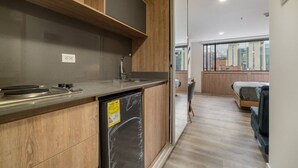 A compact kitchen with wooden cabinets, a built-in dishwasher, and a window overlooking a cityscape. - Go Living 1307 · 13th floor Loft with kitchenette, AC, GYM &co-work (Medellín)