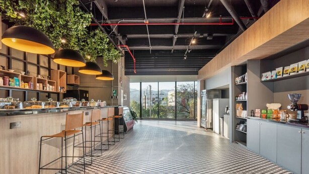 A modern kitchen with a checkered floor, bar stools, hanging plants, and a large window offering a city view.