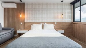 A modern hotel room with a large bed, wooden panel walls, and a view through a window.