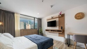 Une chambre d’hôtel moderne dotée d’un grand lit, d’un bureau, d’un téléviseur fixé au mur et offrant une vue sur le paysage urbain.