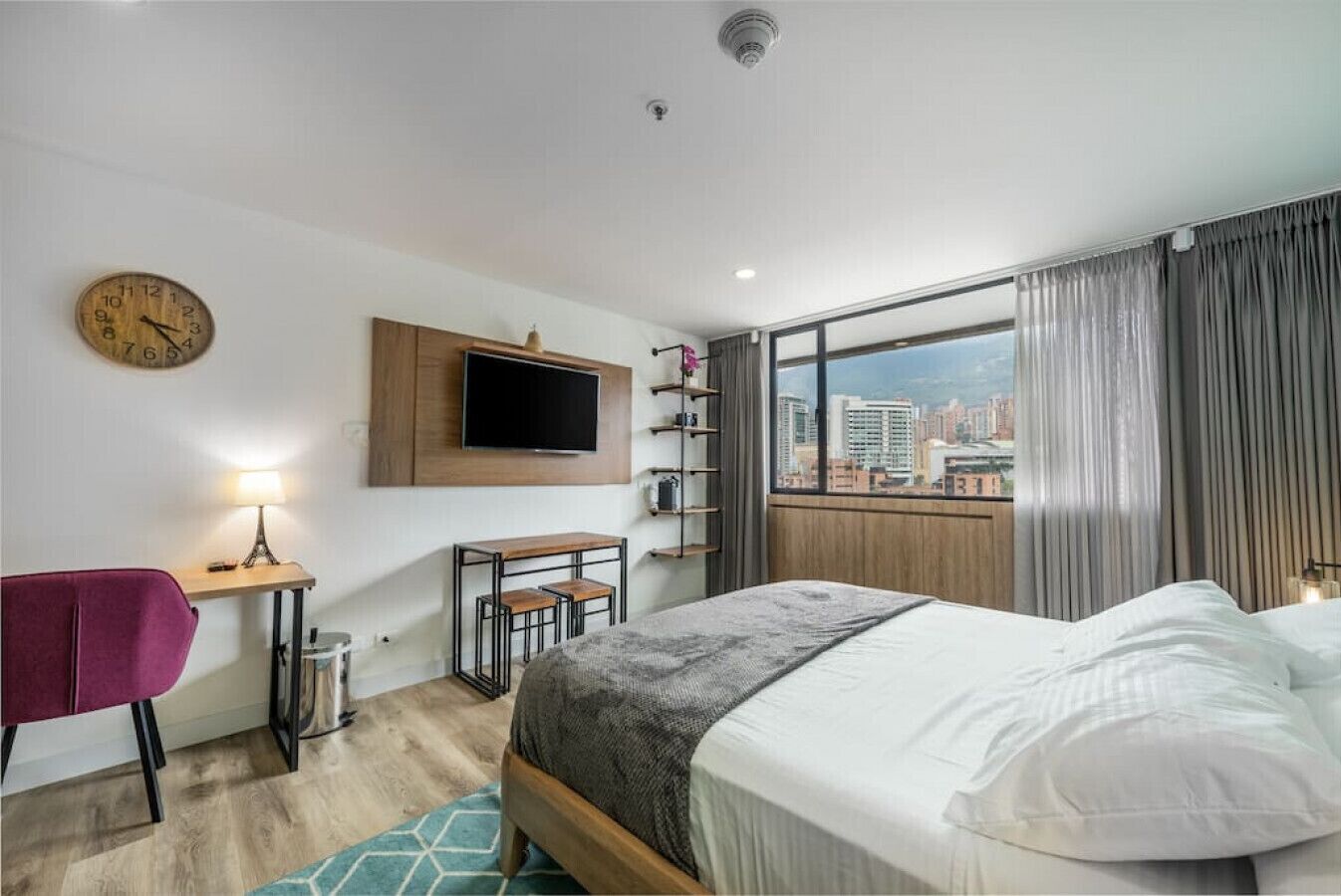 Una habitación de hotel moderna con cama, escritorio, silla, televisor y vista a la ciudad.