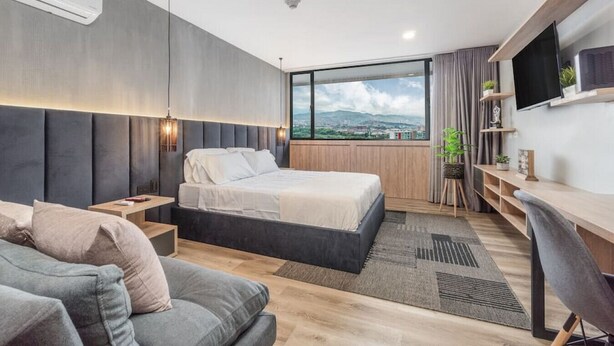 Ett modernt hotellrum med en stor säng, ett skrivbord, en soffa och utsikt över staden.
