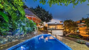A swimming pool with a stone wall and tropical plants on one side, and a modern house with a thatched roof on the other. - Casa Terracina ·  ★Amazing 5BR Mansion with private Pool &★ (Envigado)