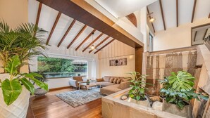A spacious living area with a high ceiling, wooden beams, a stone fireplace, and large windows offering a view of greenery. - Casa Terracina · ★Amazing 5BR Mansion with private Pool &★ (Envigado)