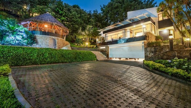 A modern house with a stone pathway leading to a thatched-roof structure and a large garage. - Casa Terracina · ★Amazing 5BR Mansion with private Pool &★ (Envigado)