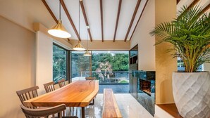 A modern dining area with a wooden table and chairs, a bench, and a large potted plant. - Casa Terracina · ★Amazing 5BR Mansion with private Pool &★ (Envigado)